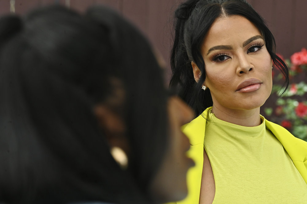 Mia Thornton wearing a yellow dress, sitting at a table, and glaring at Wendy Osefo