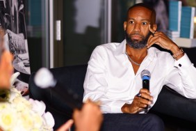 Carlos King in a white button down shirt, resting his head in his hand.