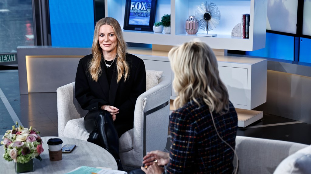 Leah McSweeney in a black sweater sitting on the set of Fox & Friends, Ainsley Earhardt is sitting across from her with her back to the camera