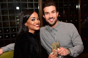 Rachel Lindsay in a black dress smiling and cheers a glass of champagne with Bryan Abasolo, who is wearing a grey shirt