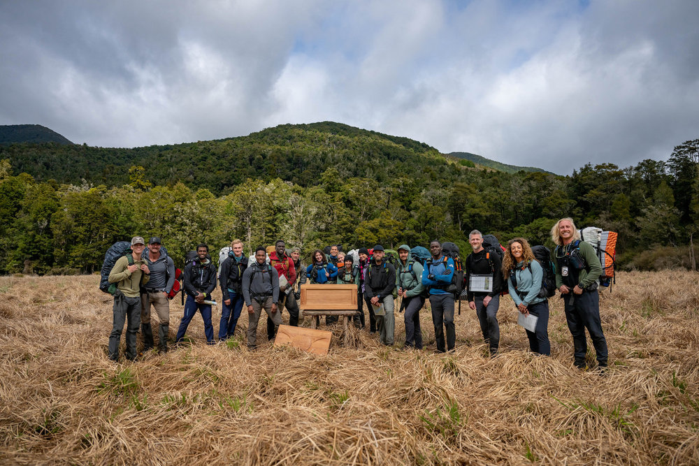 The cast of Race to Survive: New Zealand standing next to a wooden crate in the middle of a field 