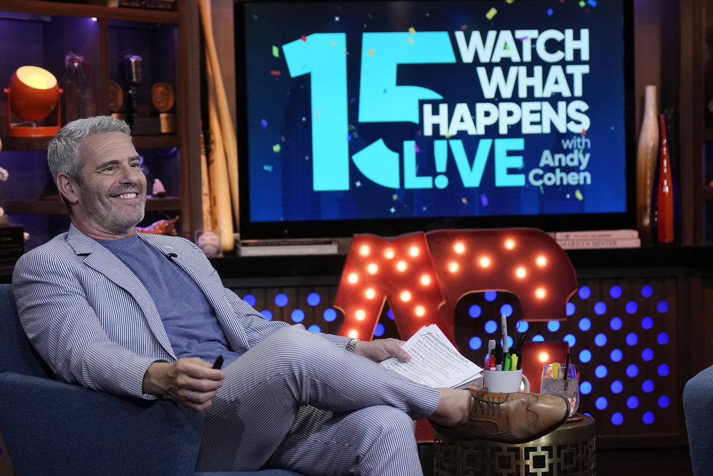 Andy Cohen in a grey suit on Watch What Happens Live, sitting with his legs crossed 