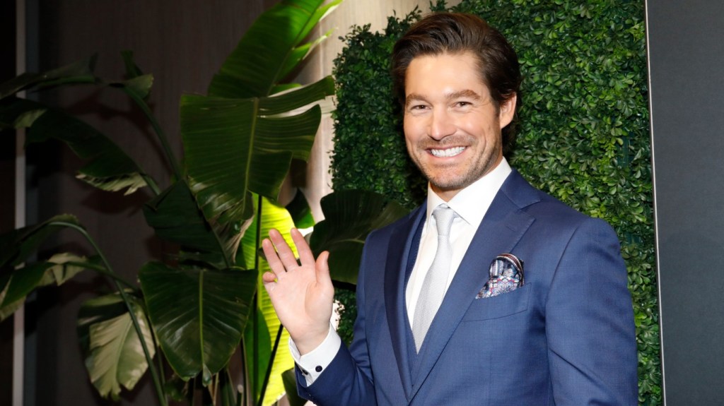 Craig Conover smiling and waving; he's wearing a navy blue suit