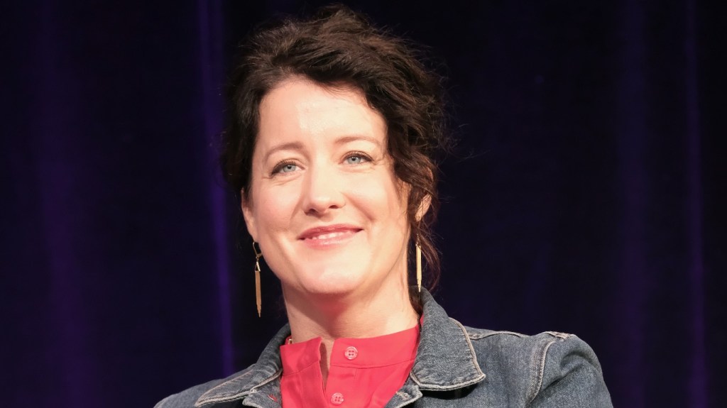 Naomi Pomeroy smiling in front of a purple backdrop