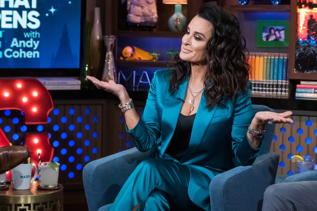 Kyle Richards in blue suit on Watch What Happens Live with her arms in the air