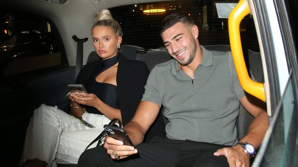 Tommy Fury and Molly-Mae Hague sitting in the back of a car looking at their phones