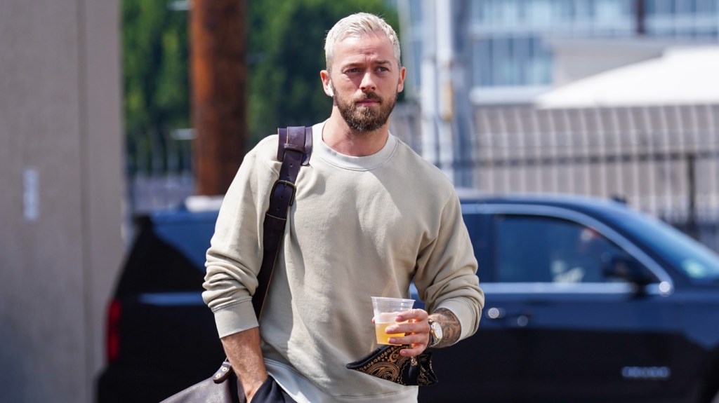 Artem Chigvinstev walking in a grey sweater and holding a beverage