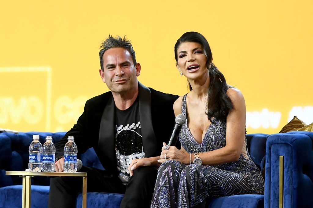 Luis Ruelas and Teresa Giudice sitting on stage holding hands at BravoCon 2023