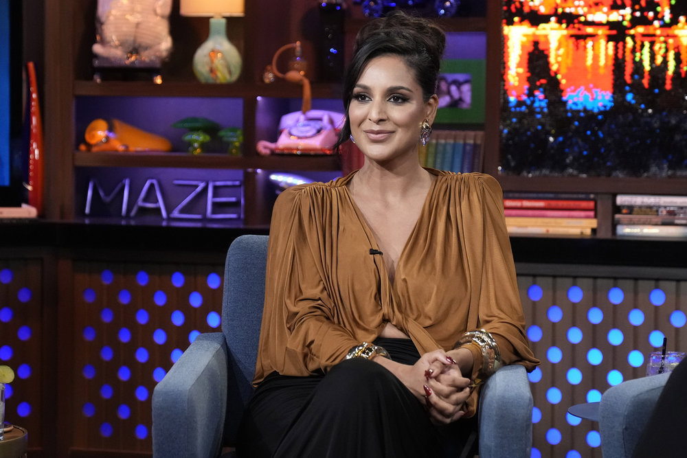 Jessel Taank wearing a gathered blouse, clasping her hands on WWHL