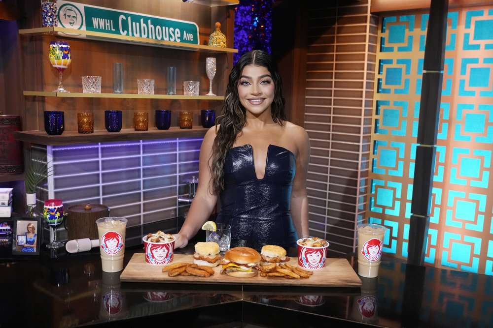 Gia Giudice on Watch What Happens Live standing in front of a a bunch of food from Wendy's.