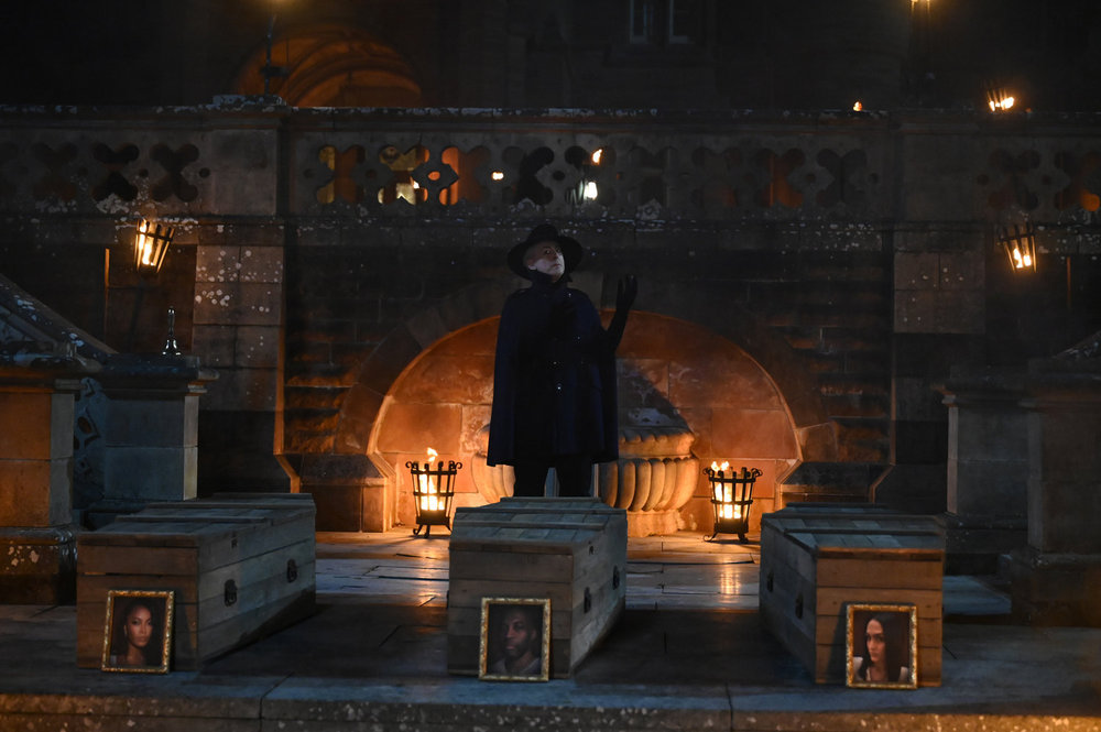 Alan Cumming on The Traitors standing in front of three coffins 