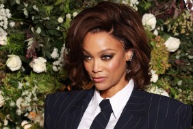 Tyra Banks in a suit posing in front of green and white flowers