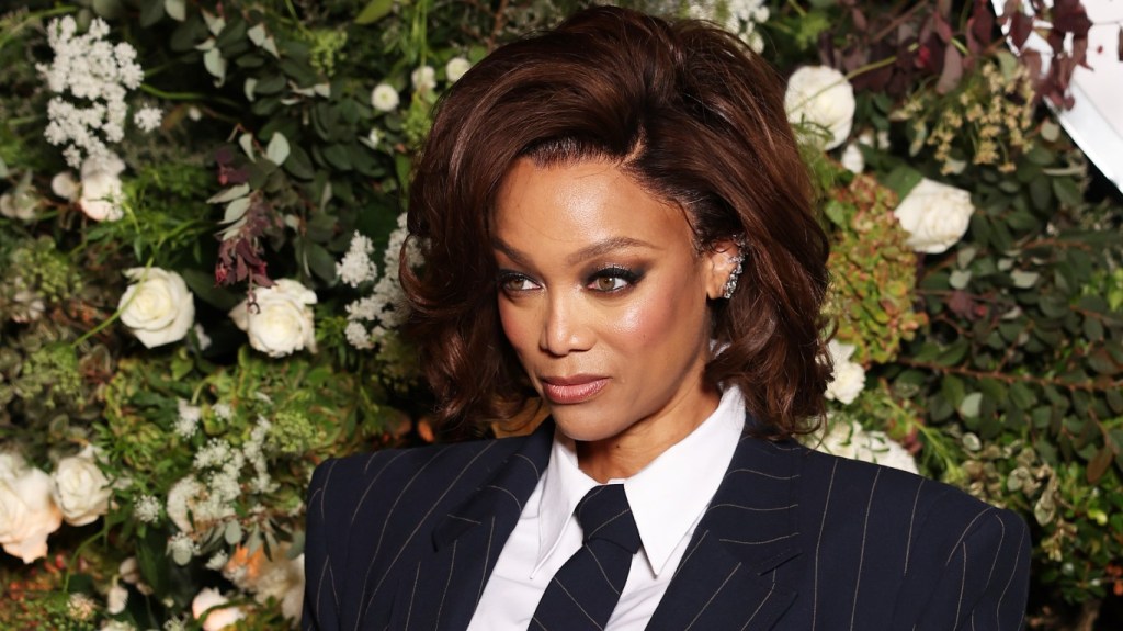 Tyra Banks in a suit posing in front of green and white flowers